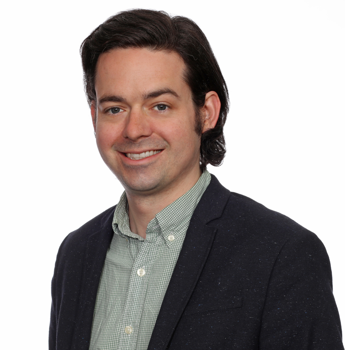 Man with dark hair wearing a dark blazer and white collared shirt.